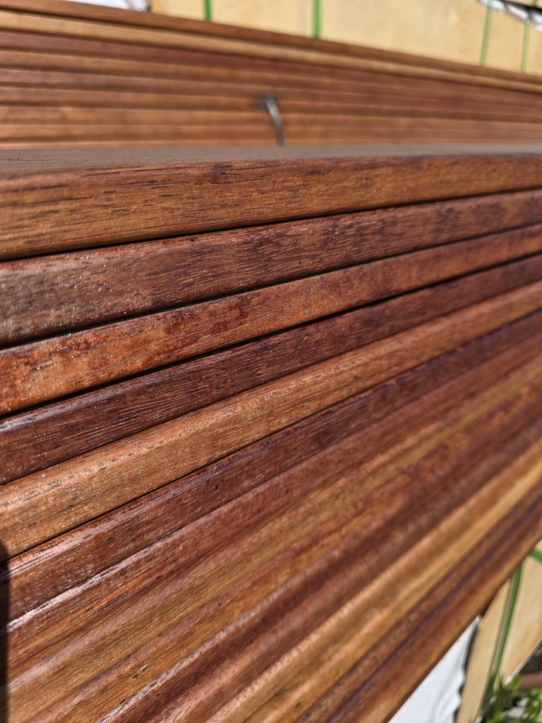 Close-up of stacked reddish-brown wooden planks with visible grain and smooth finish.