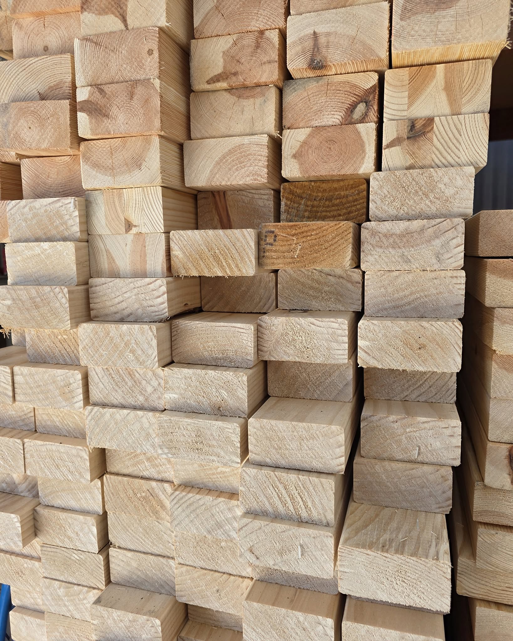 Stack of rectangular wooden planks neatly stacked, showing growth rings and cut ends in light brown lumber