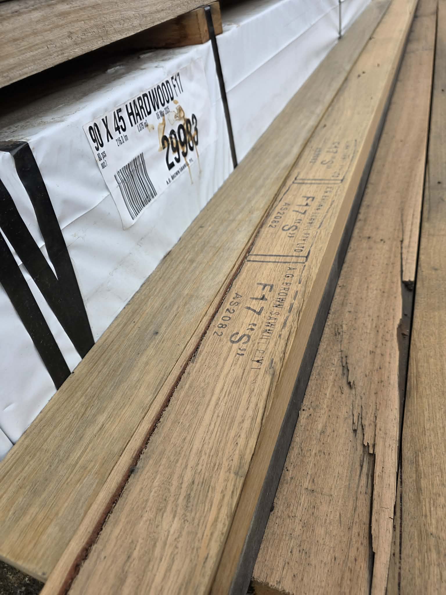 Stack of wooden floorboards with a shipping label reading '90 x 45 HARDWOOD F17' and a barcode.